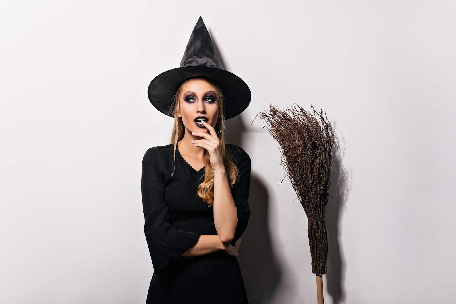 A woman wizard standing besides a broom.