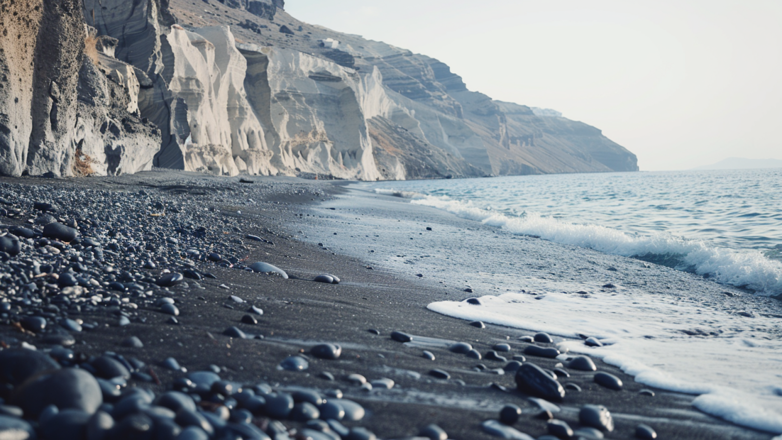 Clear waters crushing against the gray, pebbly sands of a beach in Santorini
