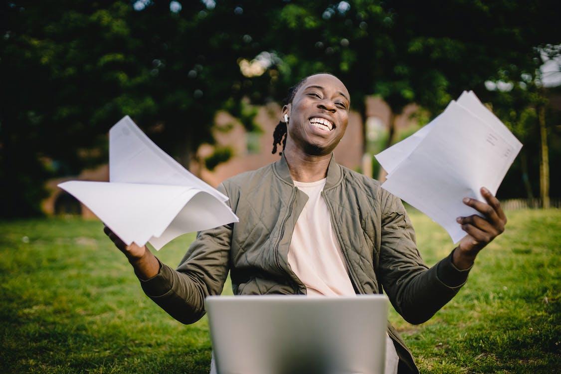 Free Happy African American man holding sheets of paper in front of laptop Stock Photo