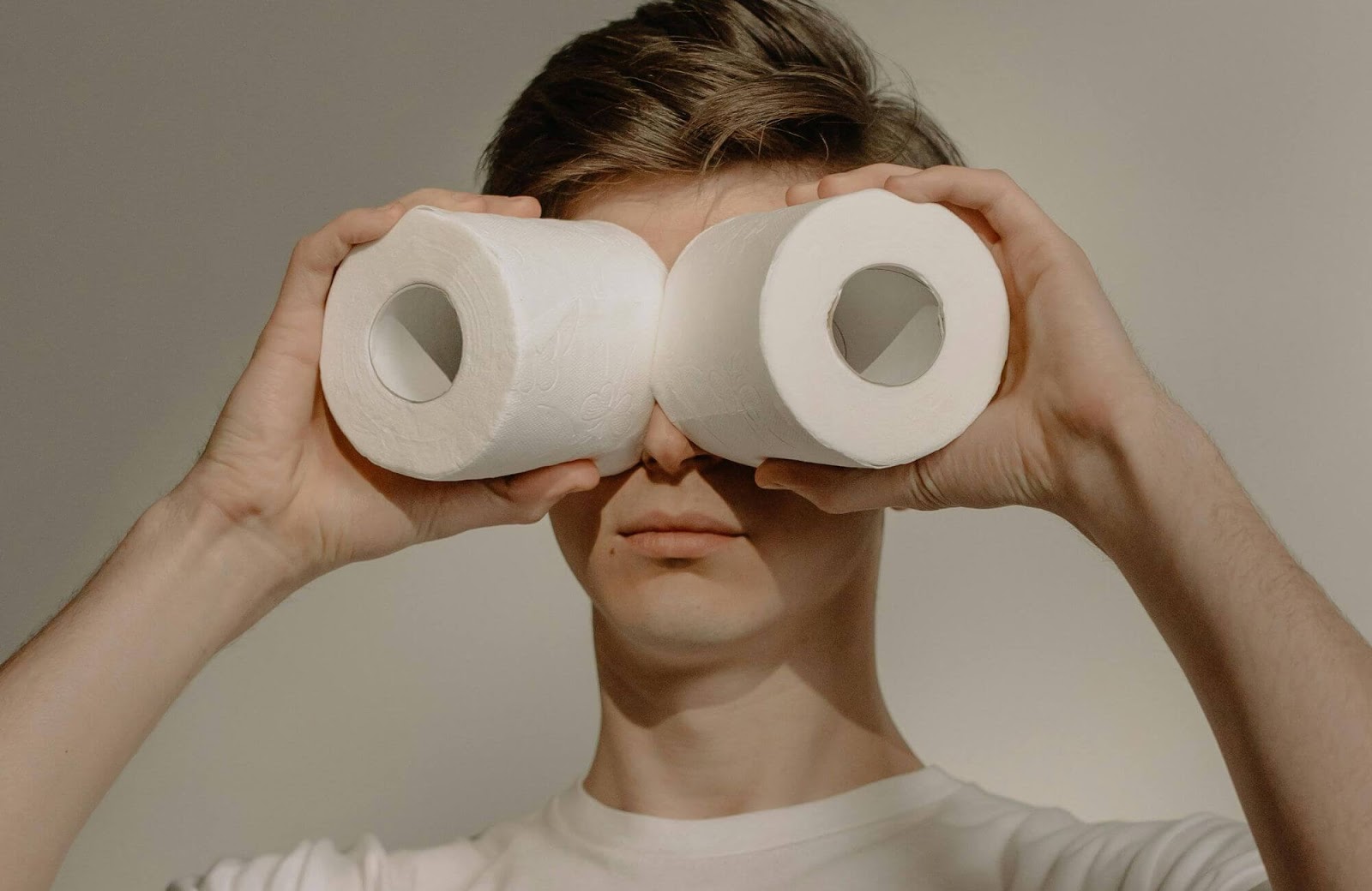 A man holding two toilet rolls up to his eyes like binoculars