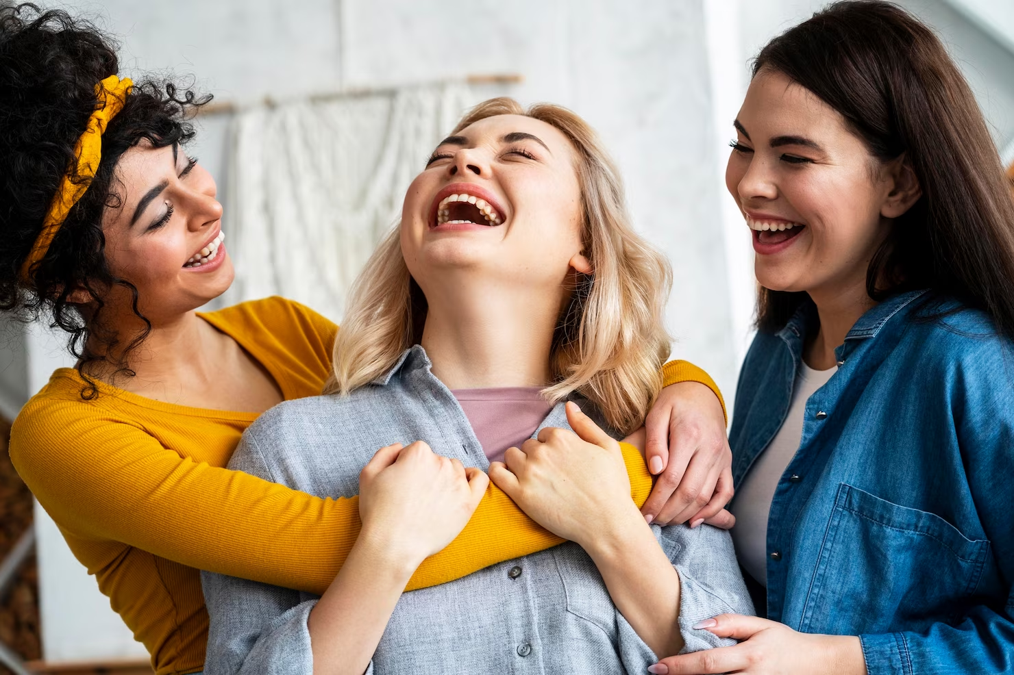 Three women laughing together discussing funny meme captions.