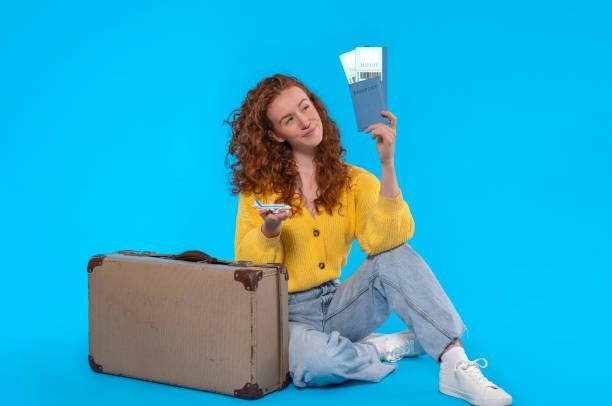 happy redhead woman in yellow jacket with a suitcase, passport,  and tickets for an airplane on a blue background.  Travel concept happy redhead woman in yellow jacket with a suitcase, passport,  and tickets for an airplane on a blue background.  Travel concept An Insurance Card Holder stock pictures, royalty-free photos & images