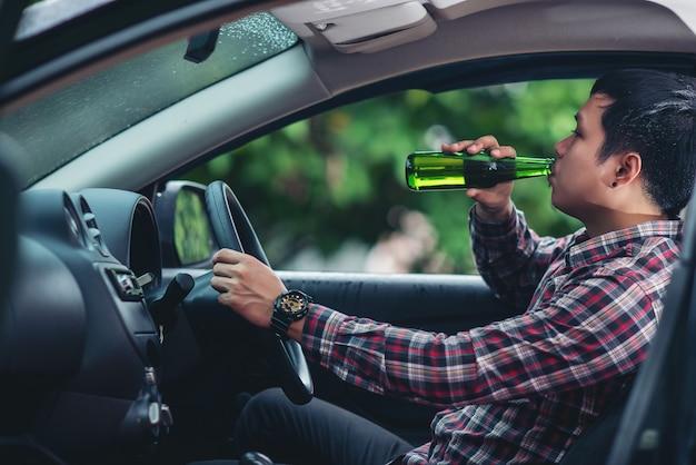 Asian man drinks a beer bottle while is driving a car