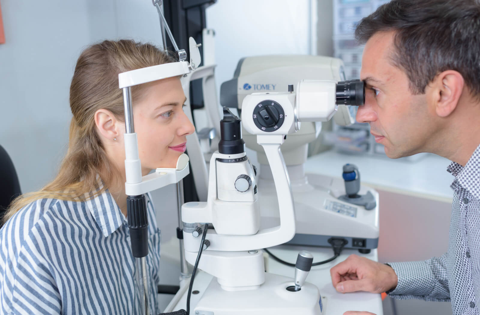 An optometrist examines his patient's eyes using a slit lamp.