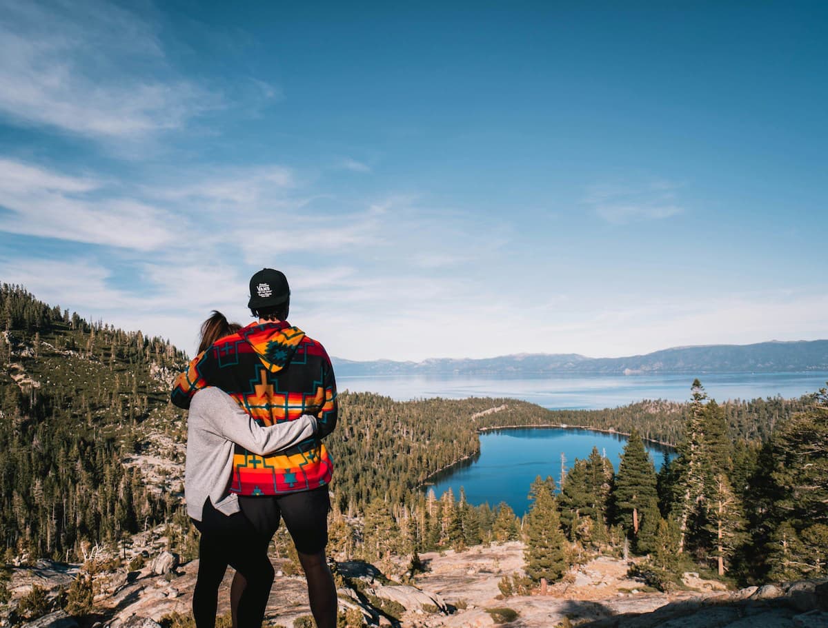 A couple hugging while on a hike in Lake Tahoe looking down at the lake and mountains in background