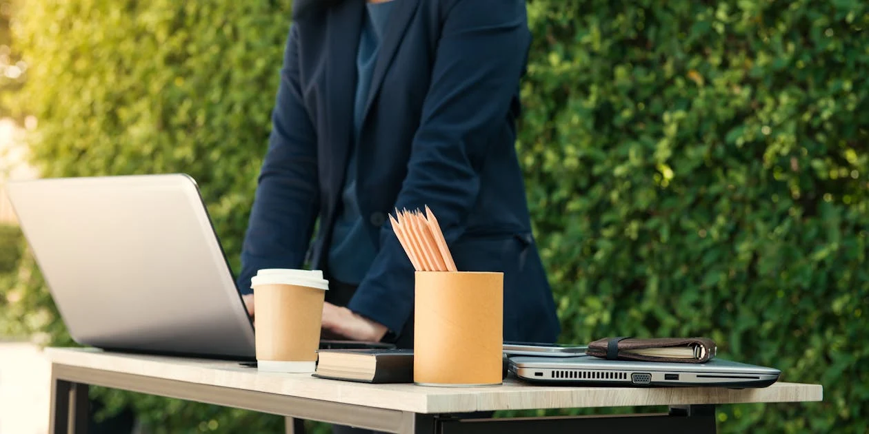 A gray laptop on a table, with a cup of pencils and a coffee cup