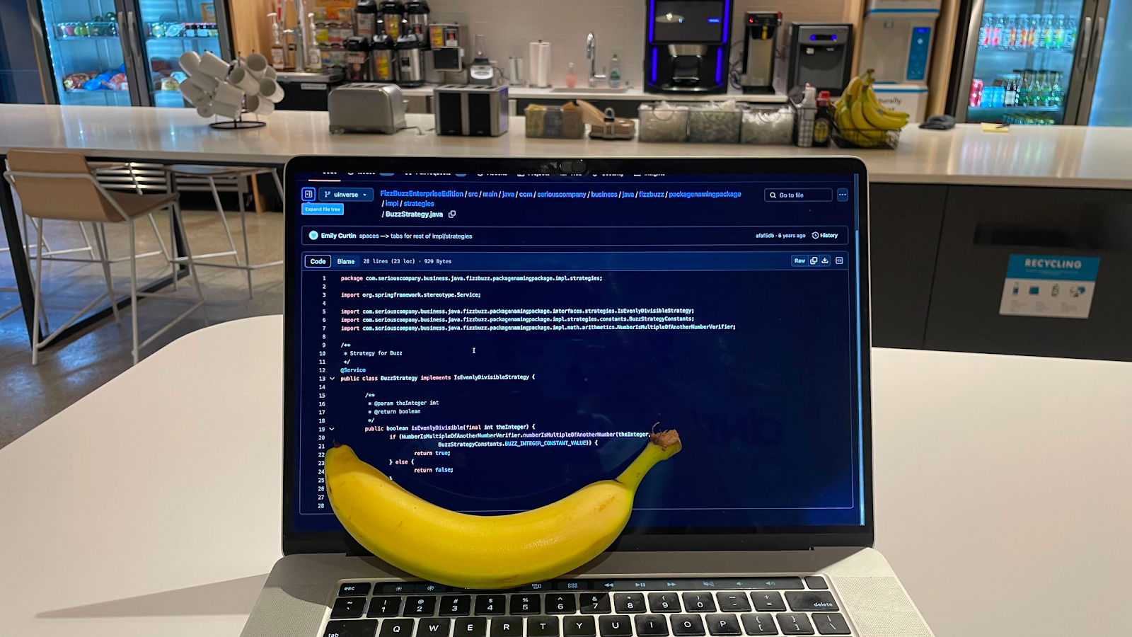 A picture of a banana sitting on a MacBook Pro screen with some code open in Github in the background.