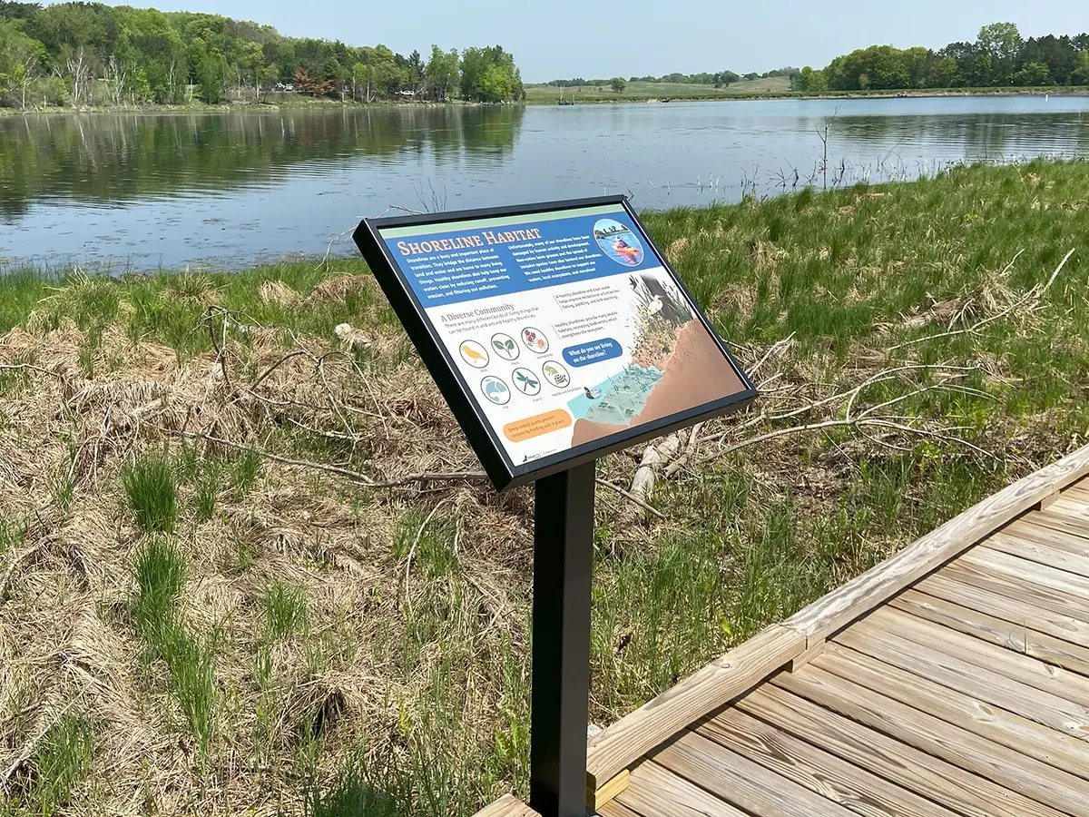 A sign on a boardwalk next to a body of water

Description automatically generated