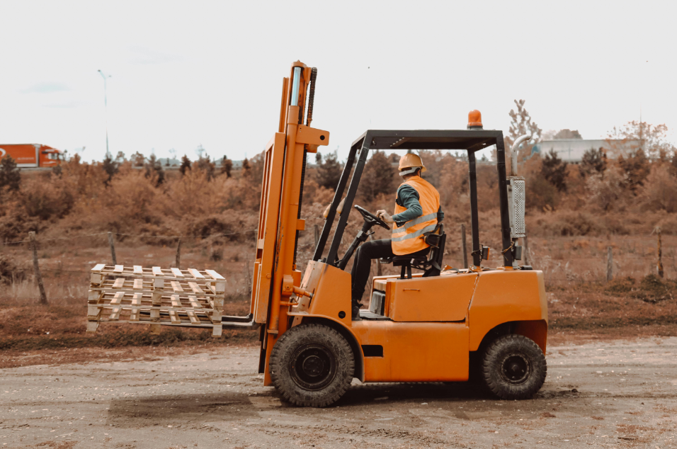 An orange forklift hauling wood pallets outdoors