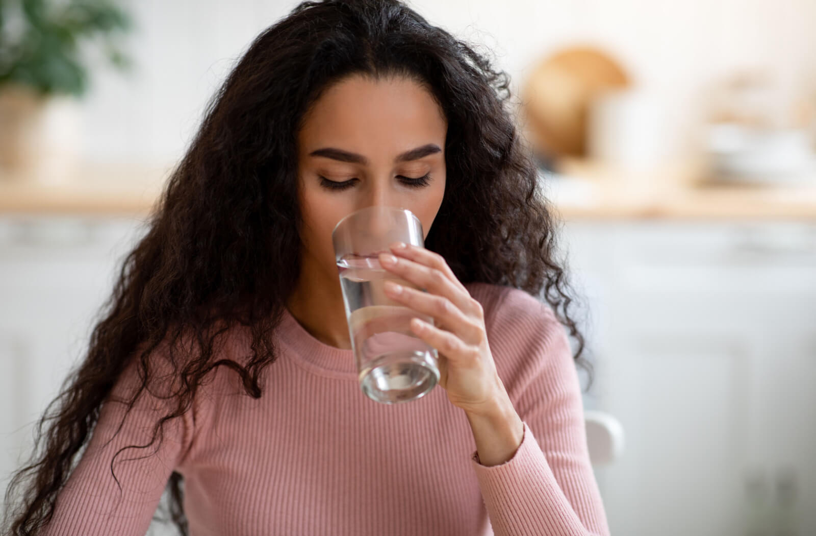 A woman with curly hair drinking a glass of water.