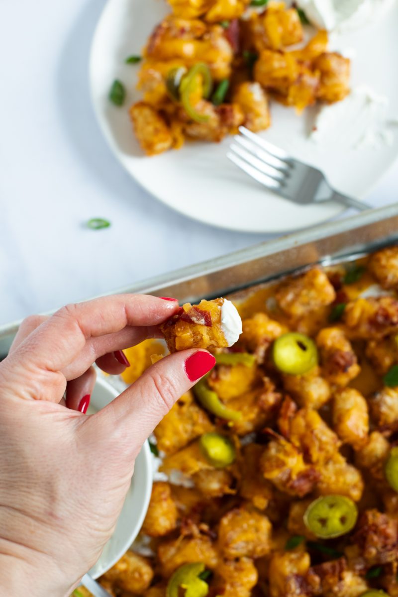 A person indulging in a bite of loaded tater tots from a tray.