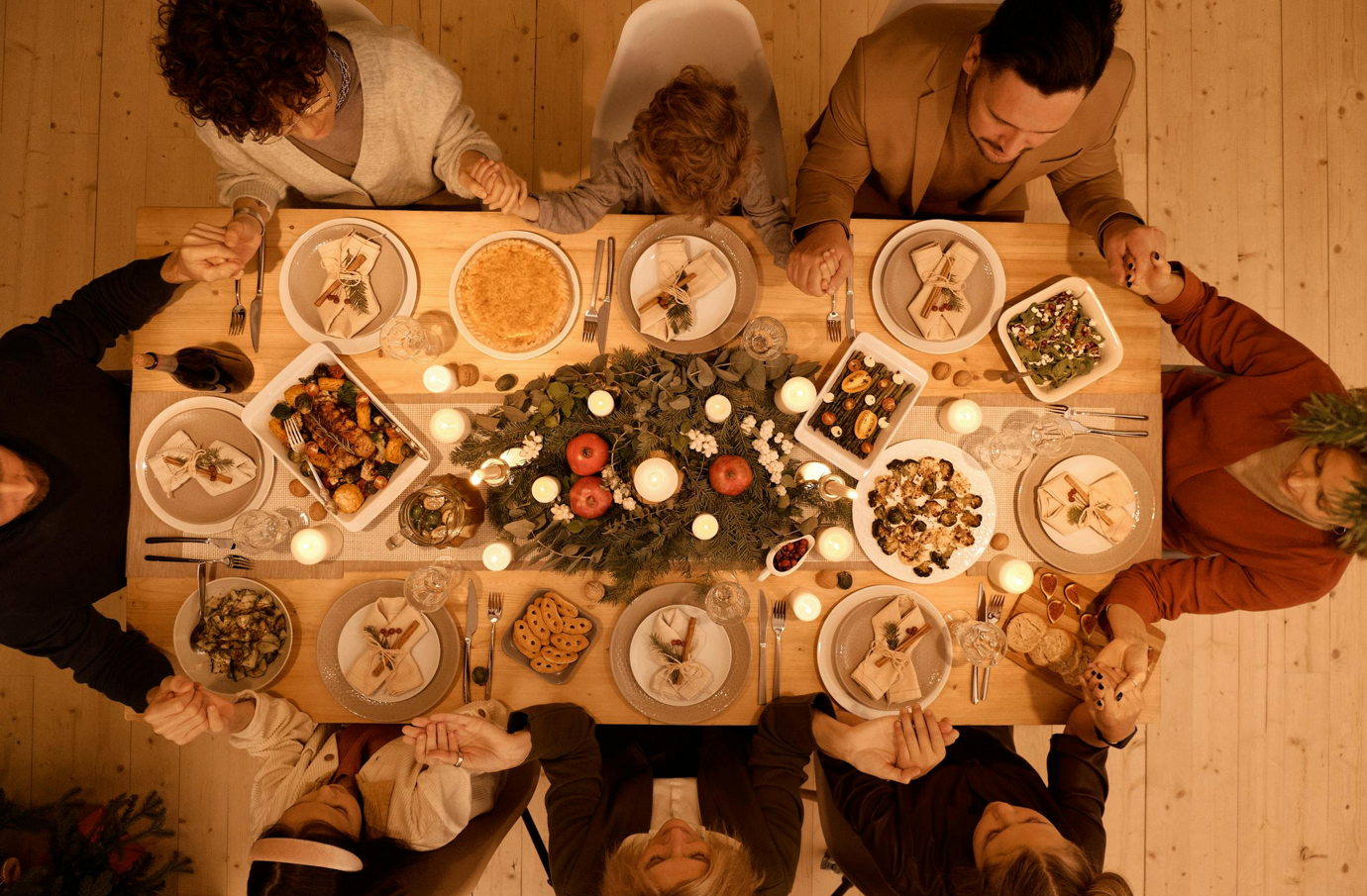 A group of people praying at a table with foodDescription automatically generated