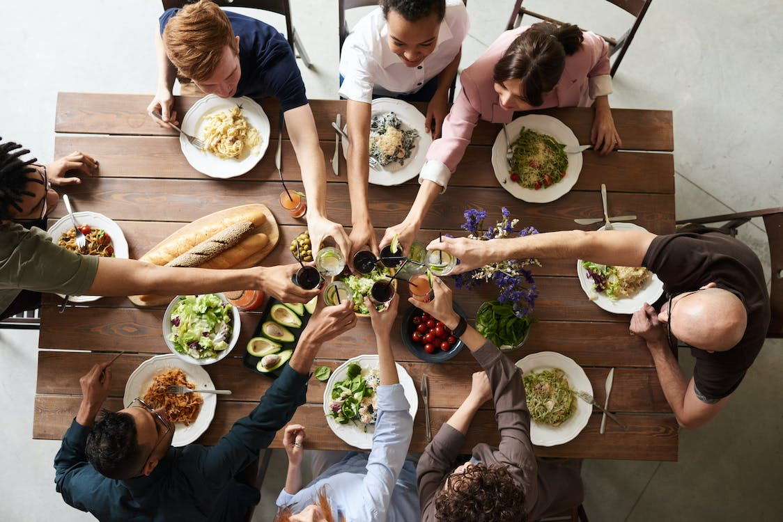 Family and friends gathered around a wooden dining table having a cheers