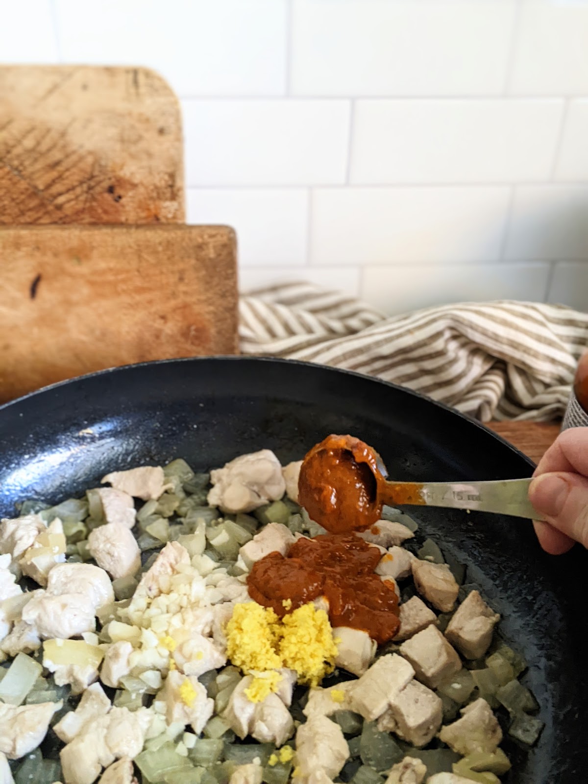 Oil, onion and garlic added to a pan with ginger, Thai red curry paste, and cooked chicken.