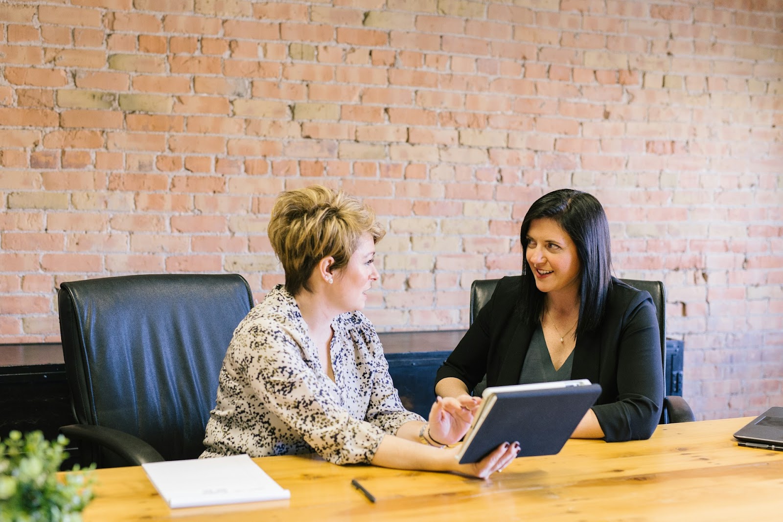 Two women sitting at a table looking at a tablet and talking