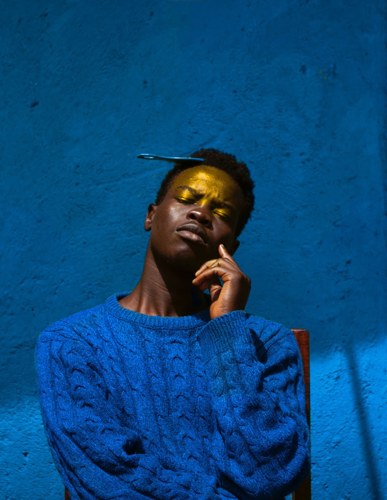 man posing in a blue sweater with gold highlight on forehead