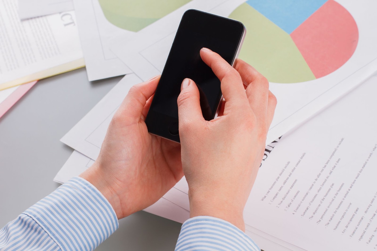 A close-up of female hands holding a mobile phone surrounded by business papers illustrates a professional environment where technology and paperwork meet.