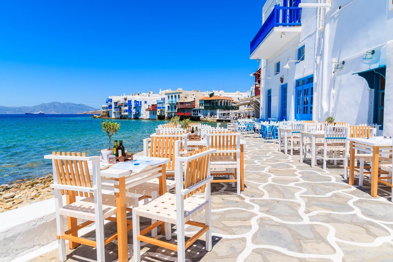 A table and chairs on a sidewalk by a body of water

Description automatically generated