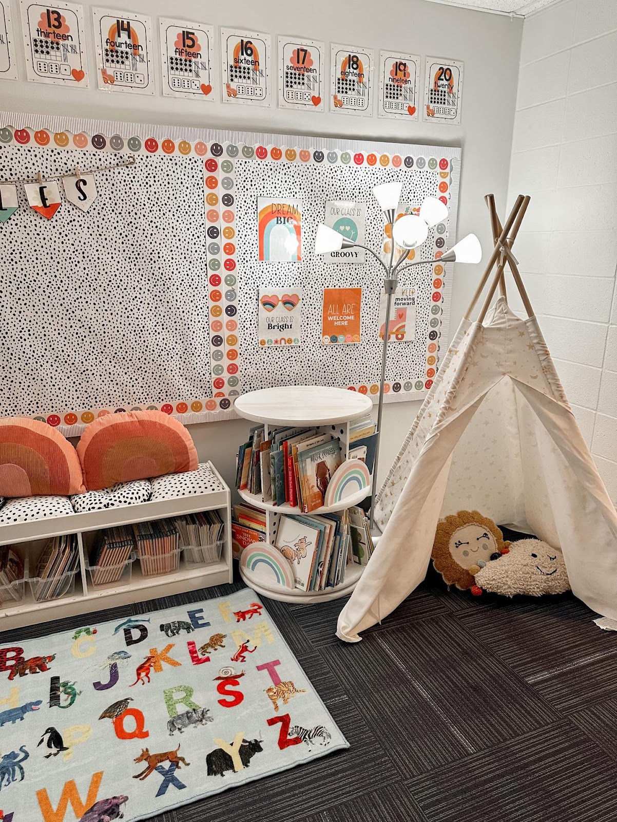 This image shows a cozy reading corner with a bench seat, buckets of books, and a tepee with pillows inside. 