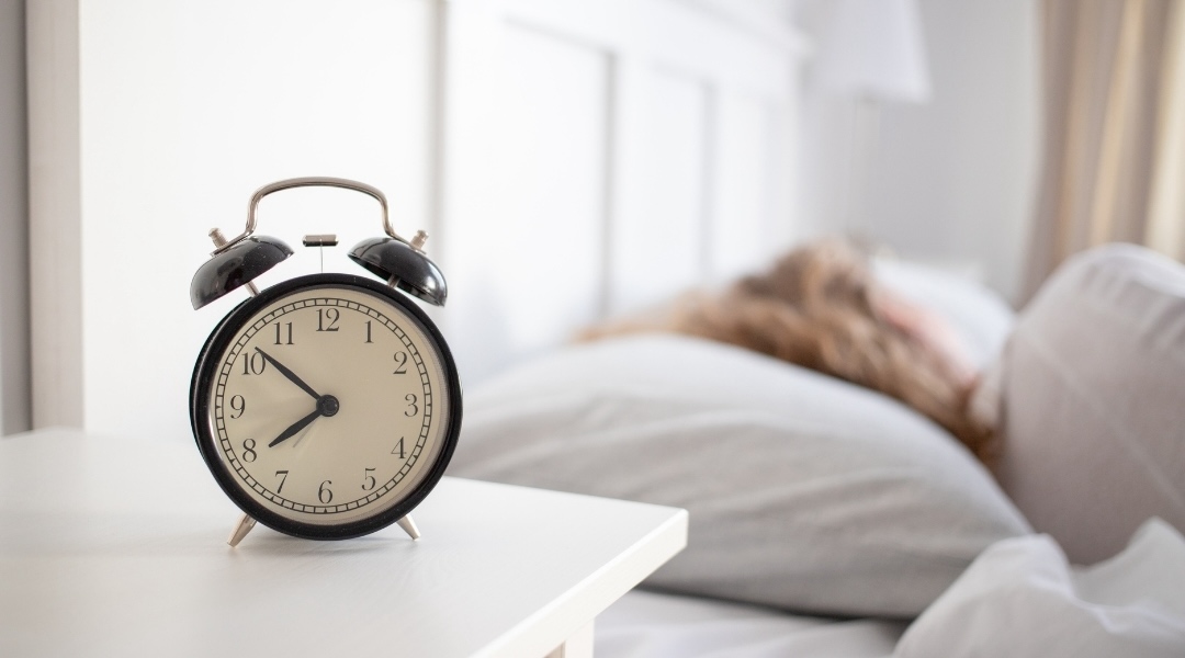 Blonde woman sleeping with a clock on the bedside table next to the bed