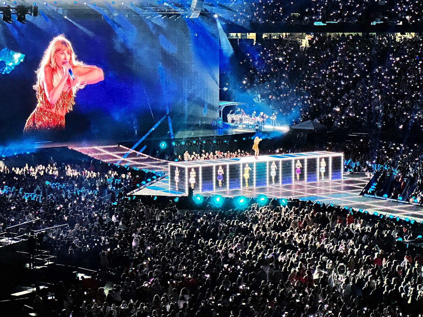 A crowd of people watching Taylor Swift perform on a stage at her The Eras Tour concert