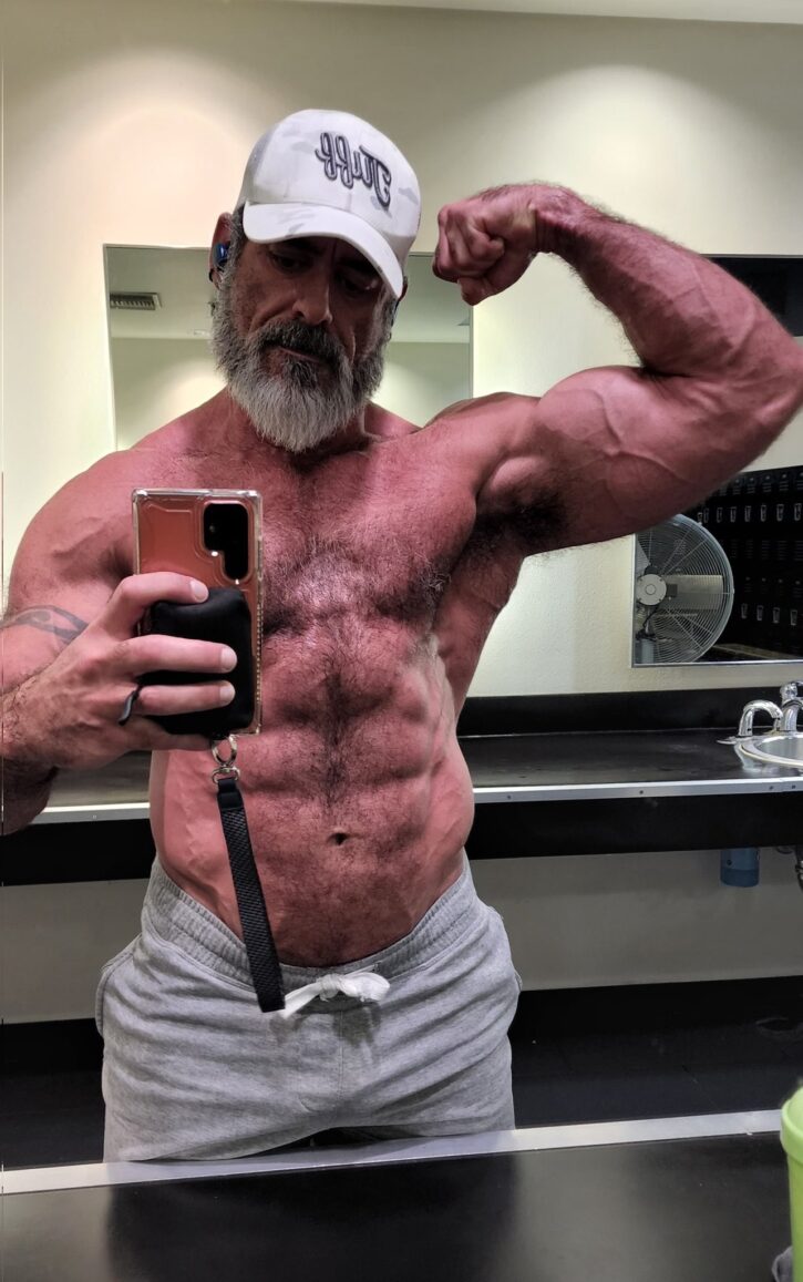 Lawson James flexing in front of the mirror at the gym shirtless wearing only grey sweatpants