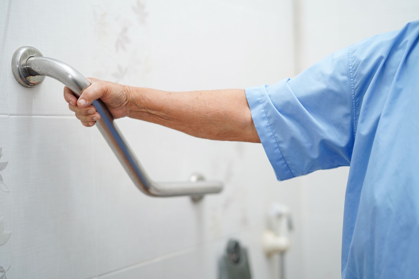 An elderly person holds a grab bar in the bathroom for support.