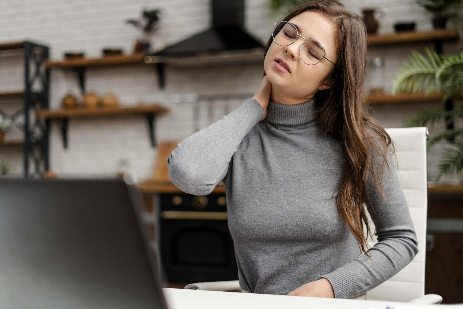 mulher em frente ao notebook com a mão no pescoço com expressão de dor