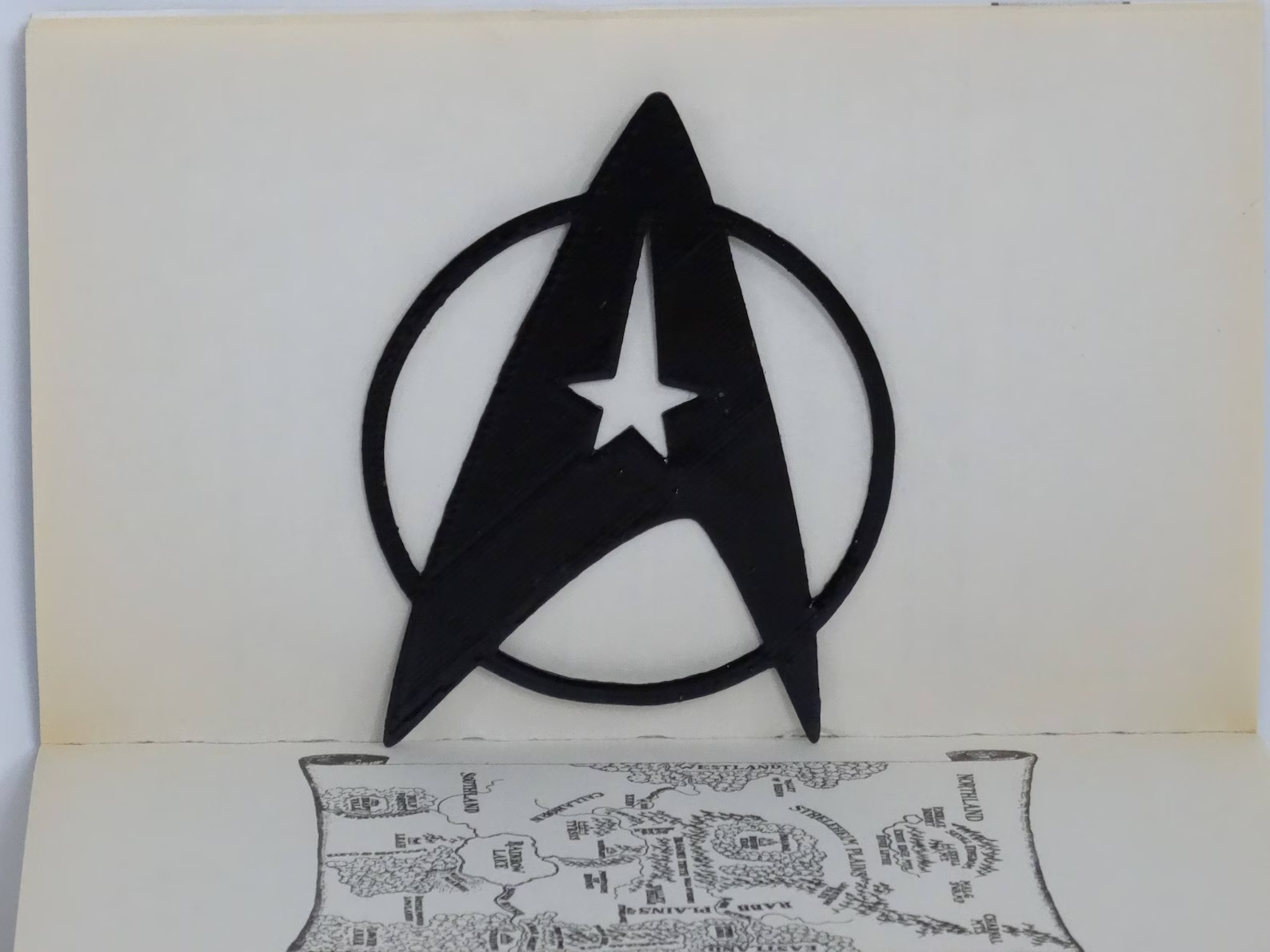 An open book with a black Star Fleet Insignia propped up against it