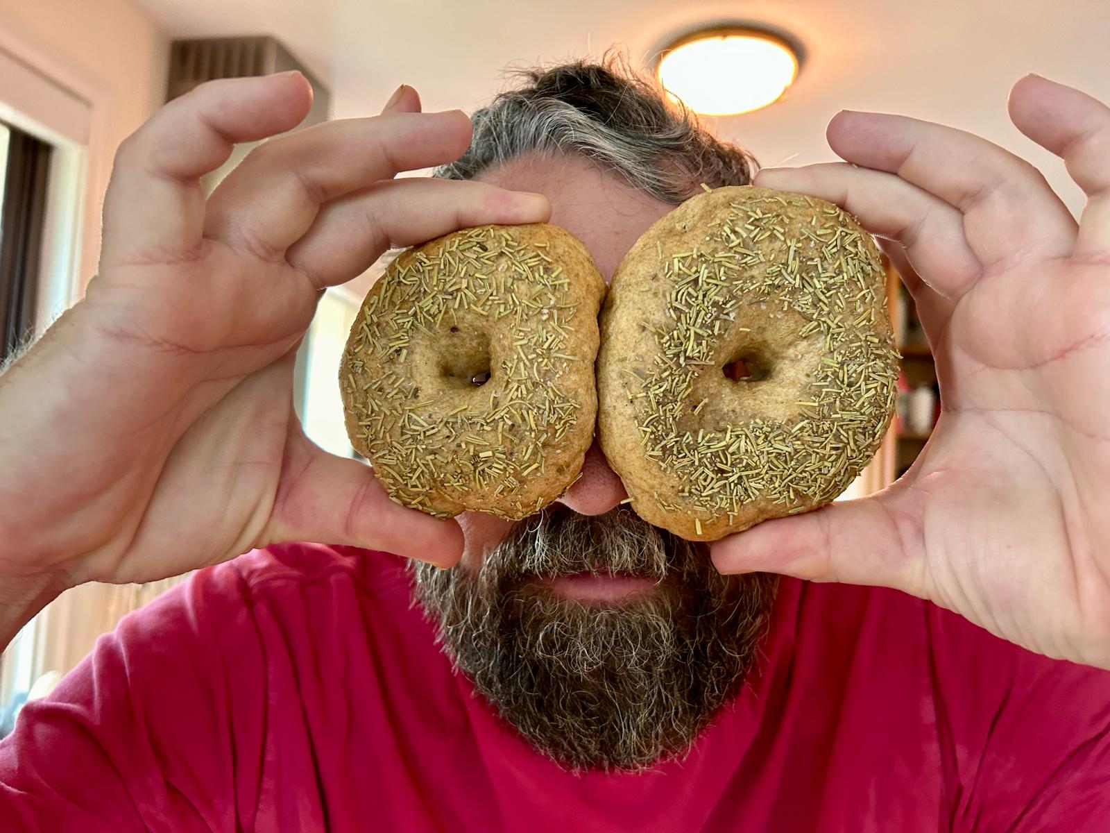 This is an image of a guy pretending that two sourdough bagels are glasses.