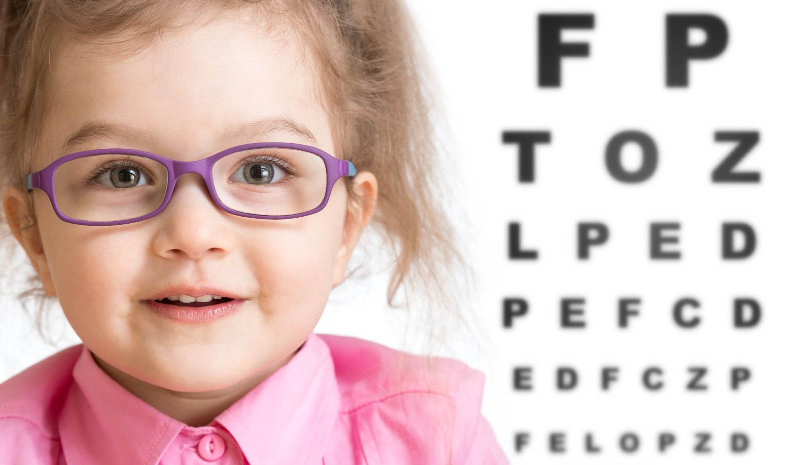 A little girl wearing eyeglasses with an eye chart in the background.
