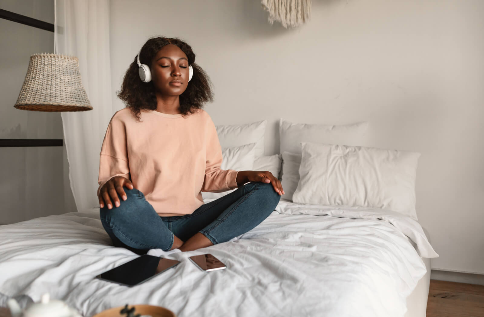A young woman meditating on a bed while wearing her headphones.