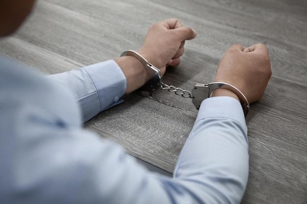 Selective focus shot of male hands in handcuffs on a wooden table