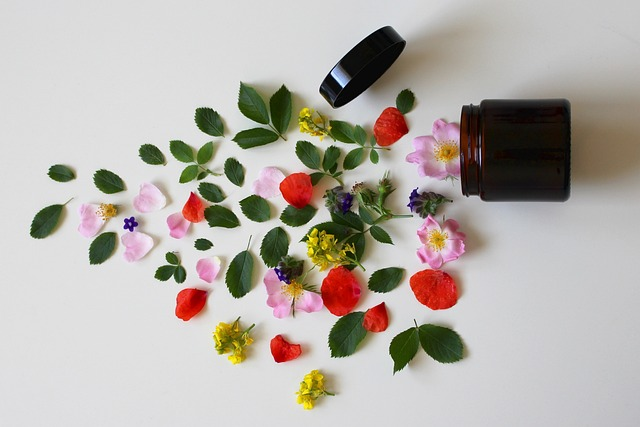 Pink,red and blue natural flowers and green leaves next to a black jar of ayurvedic cream.
