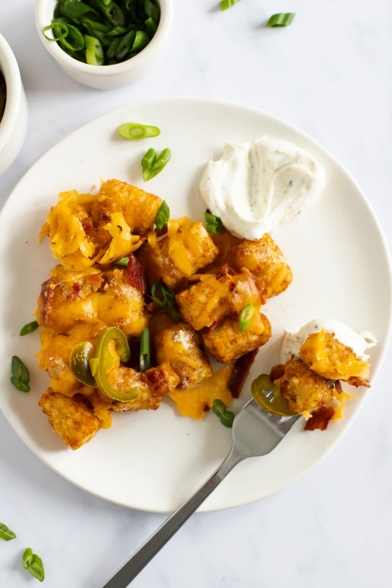 Loaded tater tots with sour cream on a plate.