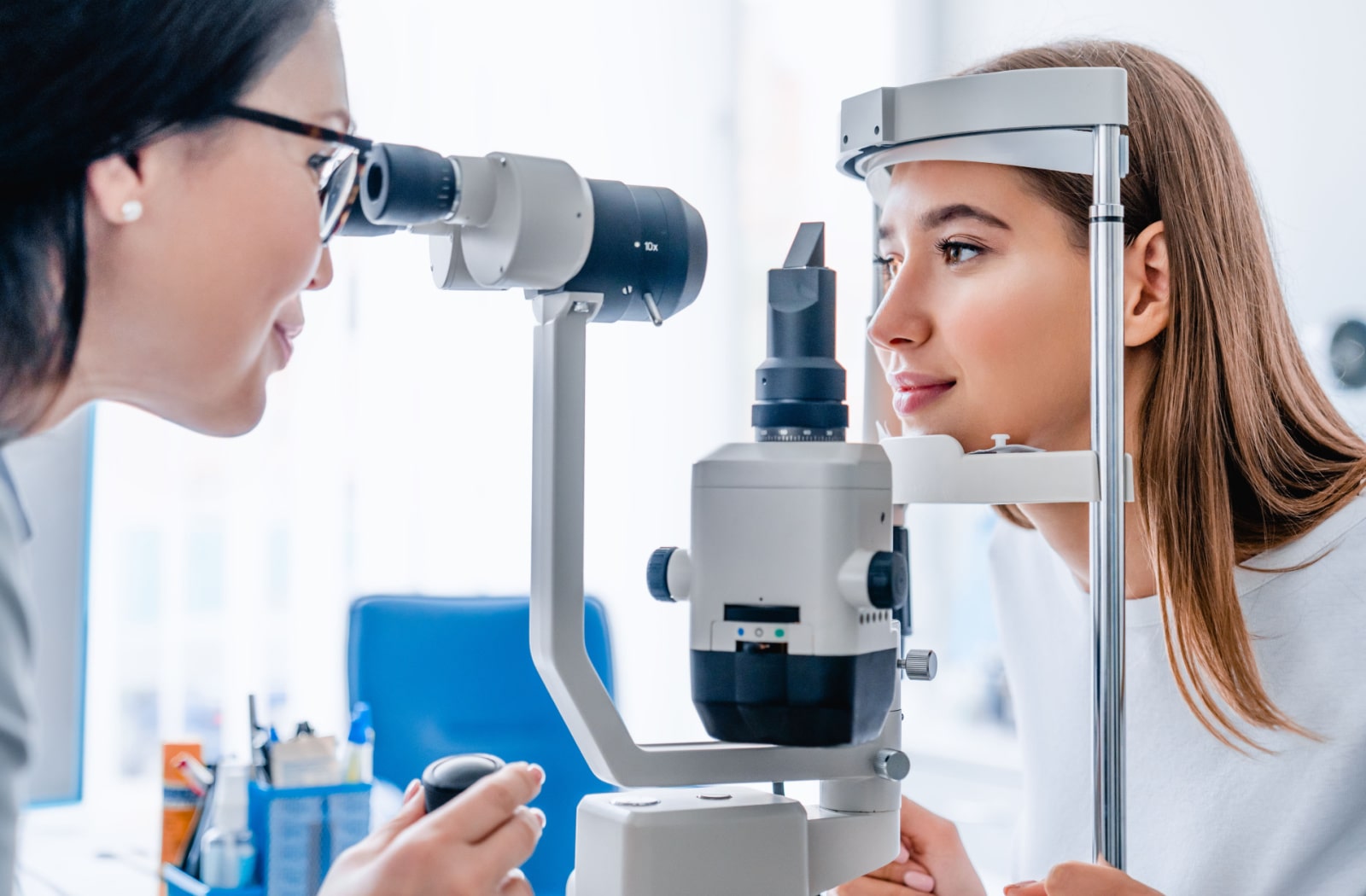 A female optometrist uses a slit lamp to examine a female patient's eyes