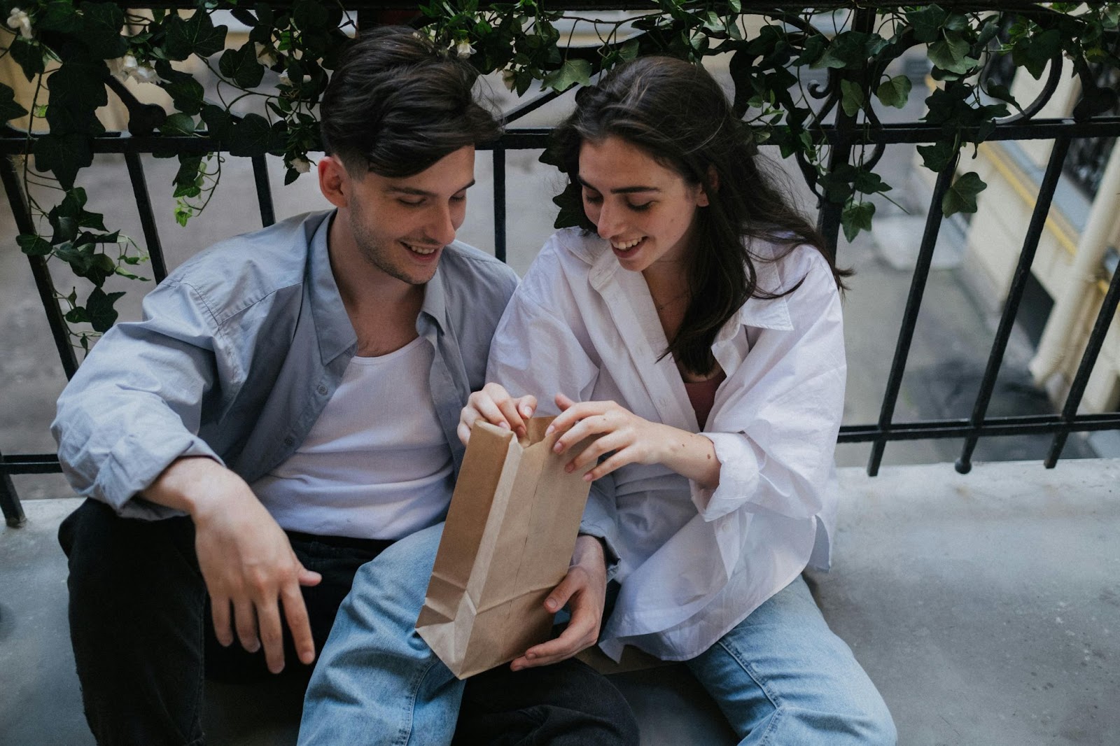Man and woman sitting together holding a brown paper bag.
