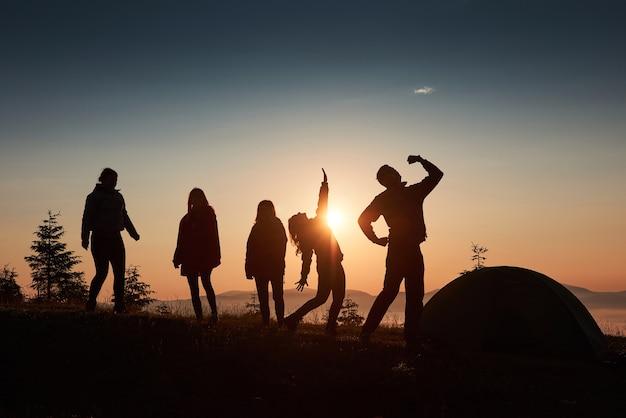 Free photo a silhouette of group people have fun at the top of the mountain near the tent during the sunset.