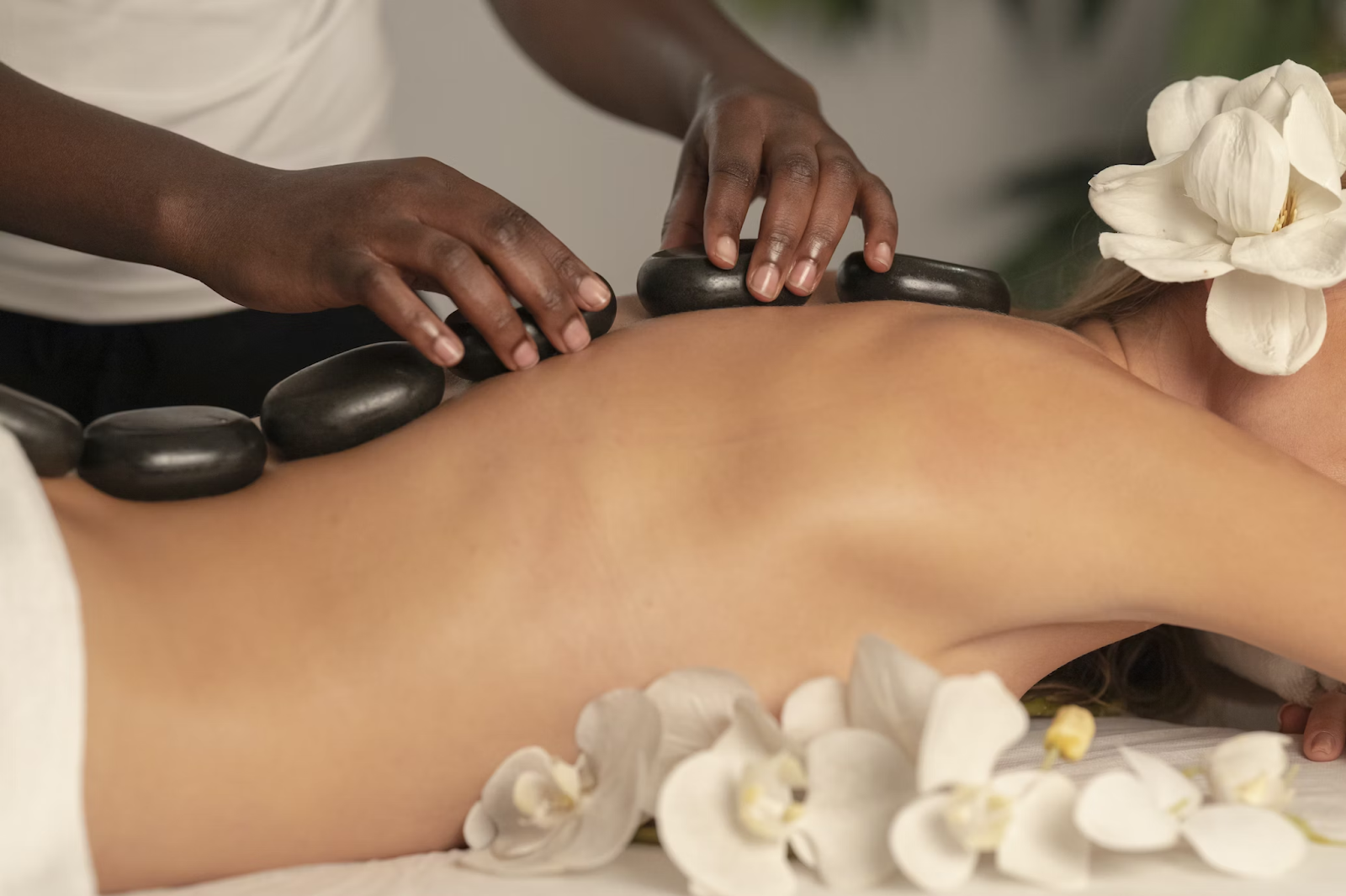 Woman getting a hot stone massage to combat stress. A massage therapist is placing the large stones in the middle of the woman's back as she relaxes.