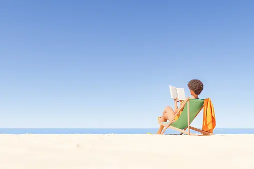 A Boy Reading a Book Sitting on a Cozy Chair at the Beach
