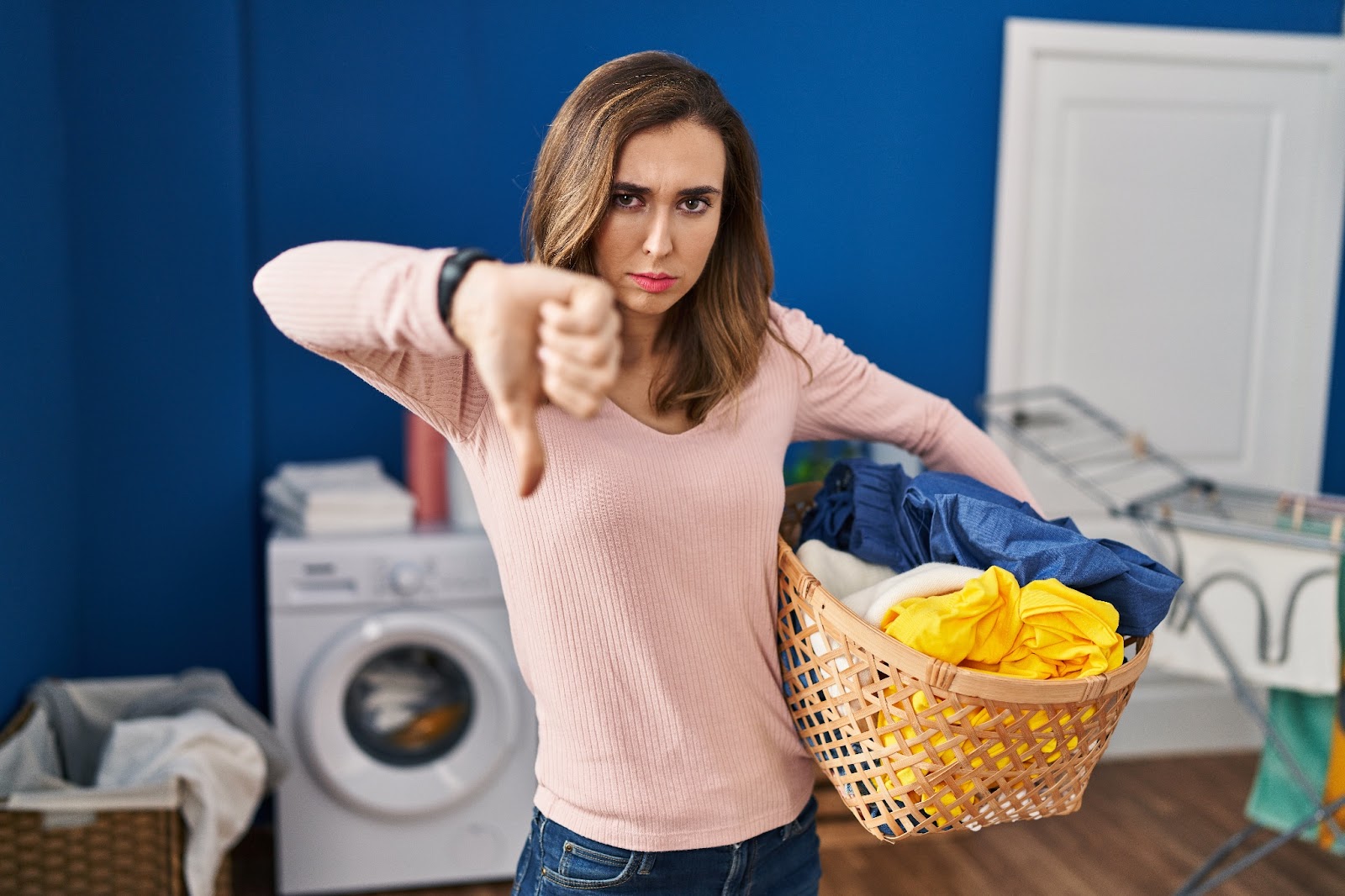 A young woman with a pile of laundry showing displeasure at her faulty washing machine 