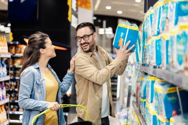 A happy parents buying diapers at supermarket. A smiling couple purchasing diapers in supermarket. adult diaper stock pictures, royalty-free photos & images