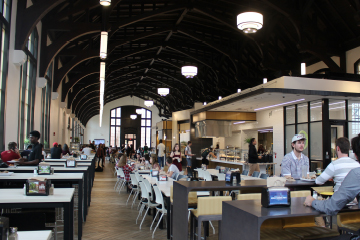 A photo of a student cafeteria with various food stations and students sitting at tables eating and socializing.