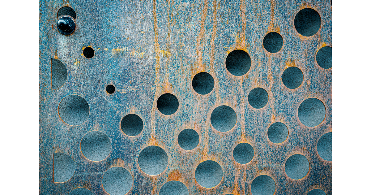 Holes, small and large, comprise several diagonal lines across a blue and brown surface, showing a greyish-blue background through each opening.