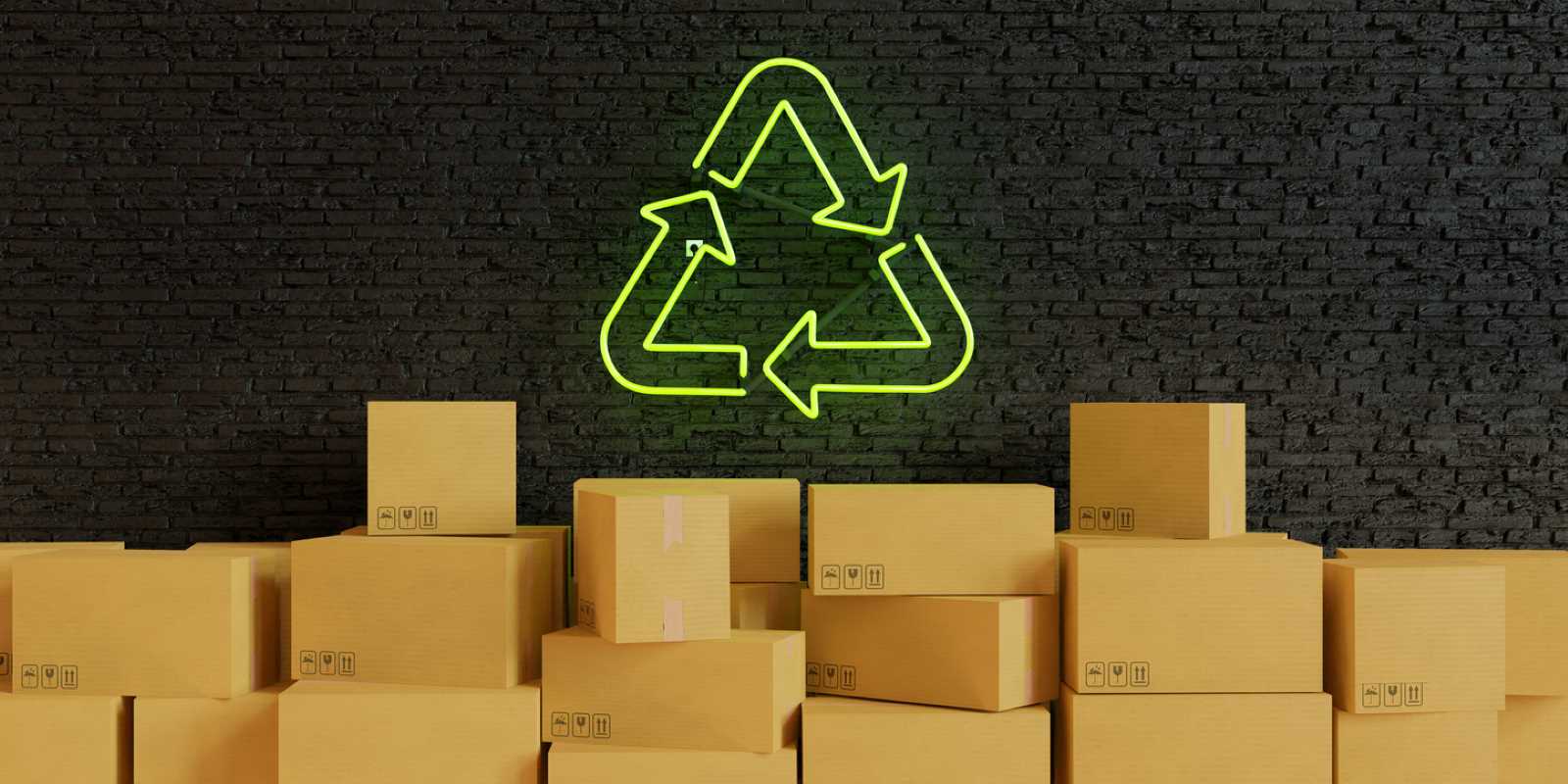 Cardboard boxes are stacked in front of a dark brick wall illuminated by a green neon recycling symbol lamp.