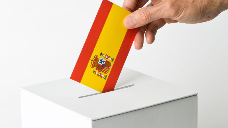 Persona ingresando una bandera española en una urna