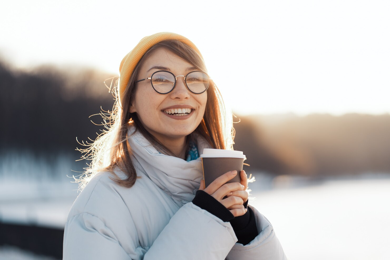 A woman laughing and holding a coffee cup in winter.