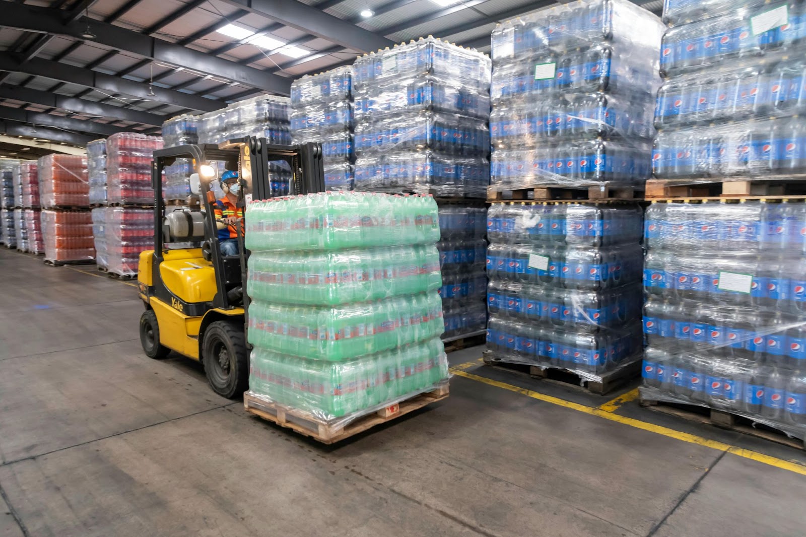 A forklift operator hauling wooden pallets of sodas