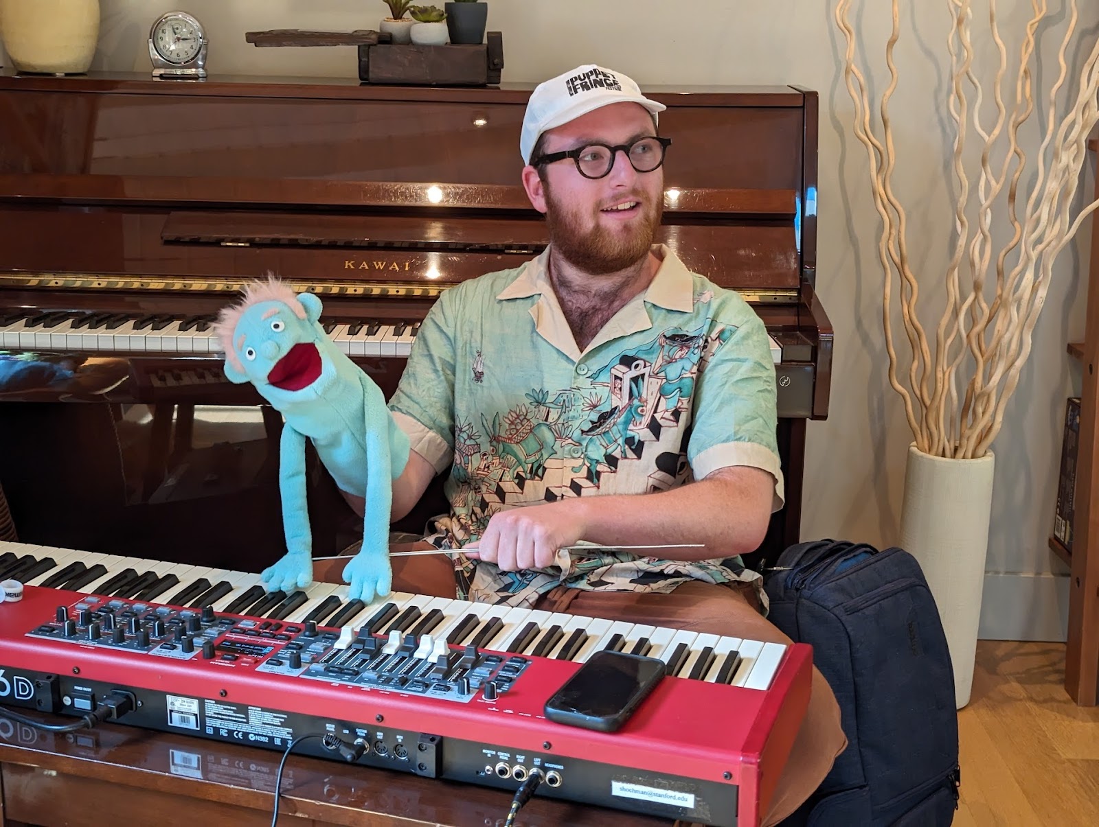 A photo of a person in front of the keyboard with a puppet in one hand.