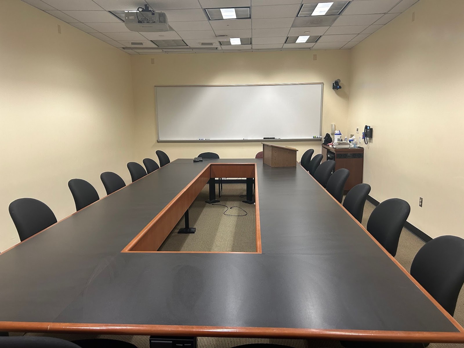 View of the front of the room: Room camera, keyboard and mouse, hotline phone, projector and screen.